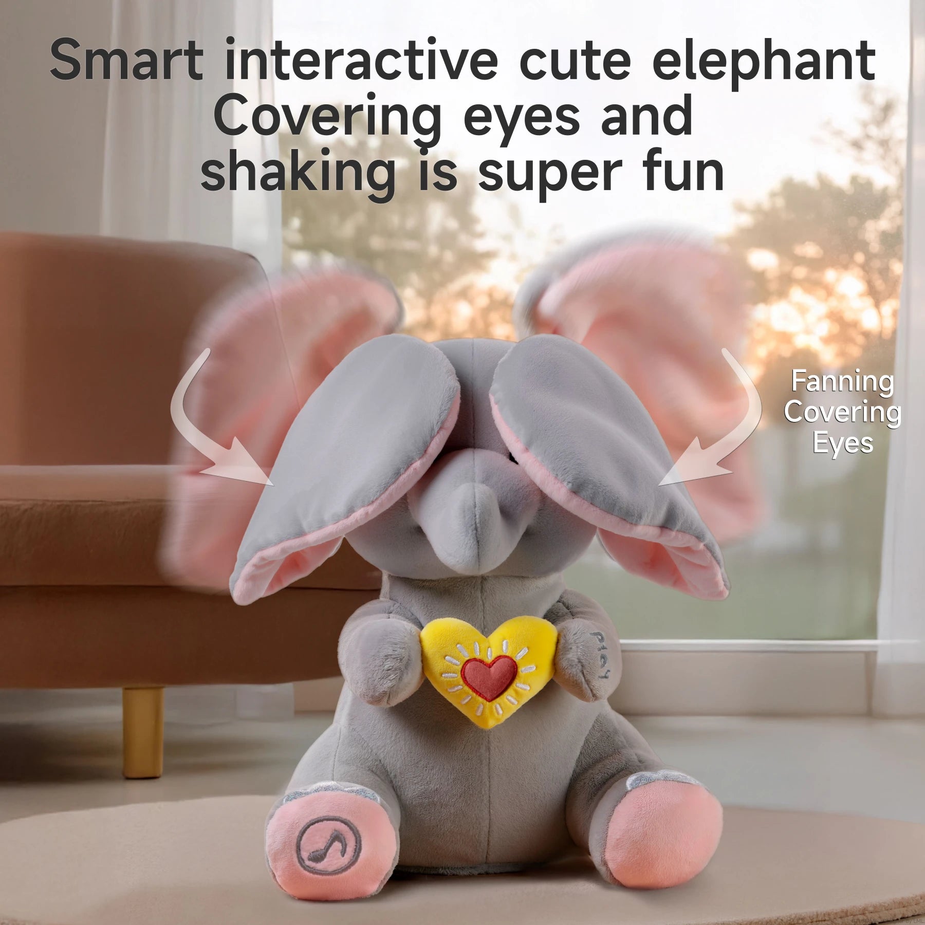 Interactive elephant plush toy with pink ears flapping to cover its eyes. The toy is holding a yellow heart with a red center, and has a 'play' label on one hand. Motion blur on the ears indicates movement. Text above reads: 'Smart interactive cute elephant – Covering eyes and shaking is super fun.' Arrows point to the ears with labels: 'Fanning' and 'Covering Eyes.'