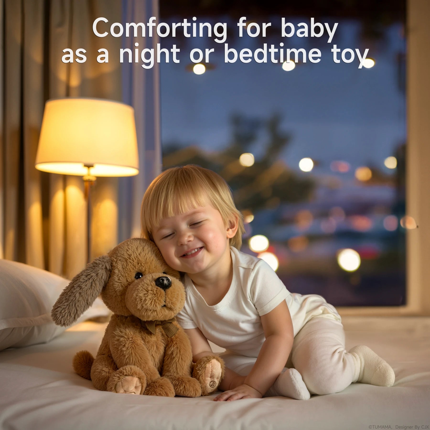 A young child in white pajamas sits on a bed at night, smiling with eyes closed while cuddling a soft brown plush puppy stuffed animal toy. The cozy bedroom is softly lit by a bedside lamp, and a window shows blurred city lights outside.