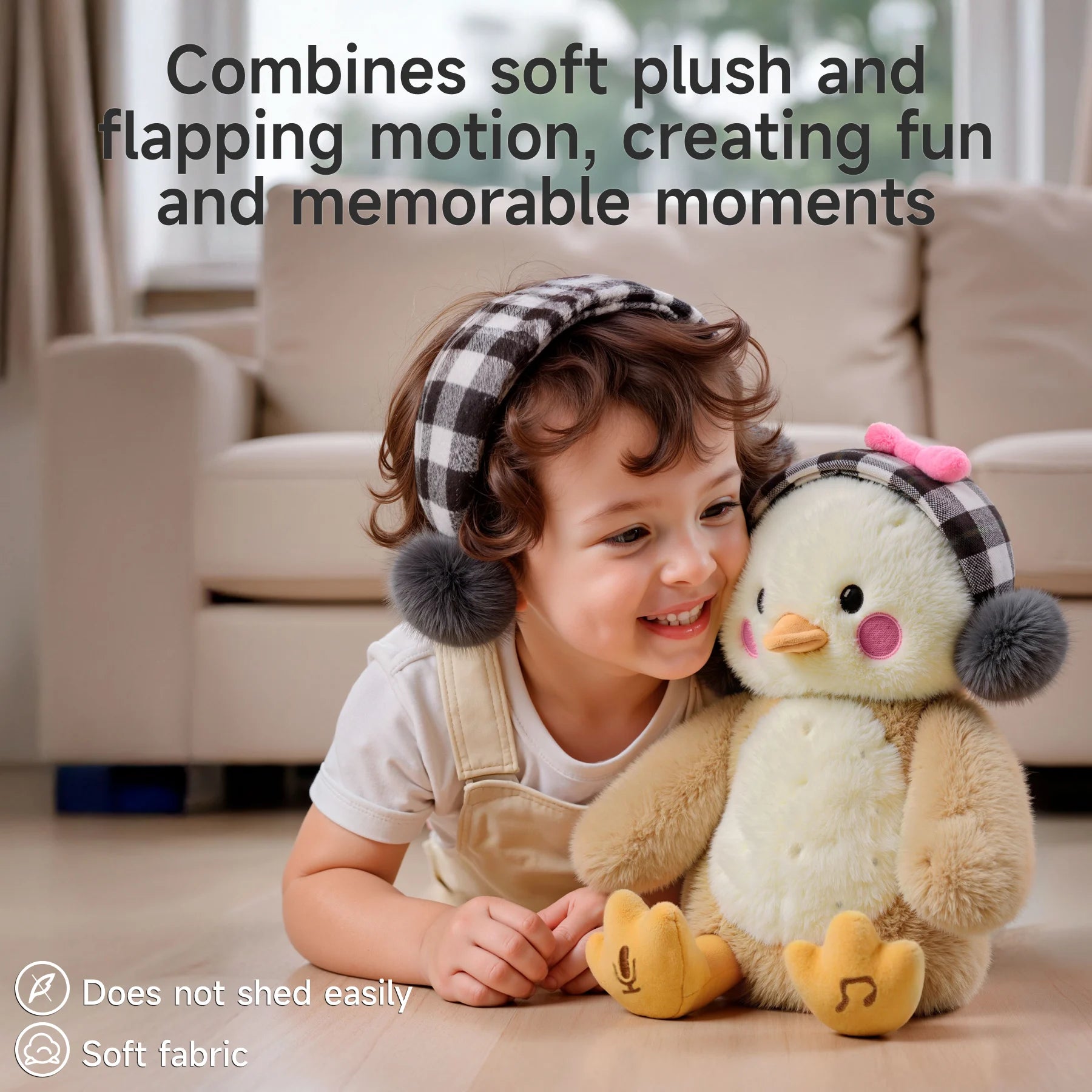 A smiling toddler lying on the floor next to a cute interactive plush chick toy with plaid earmuffs and a pink bow. Text at the top reads ‘Combines soft plush and flapping motion, creating fun and memorable moments.’ Icons at the bottom indicate ‘Does not shed easily’ and ‘Soft fabric.’