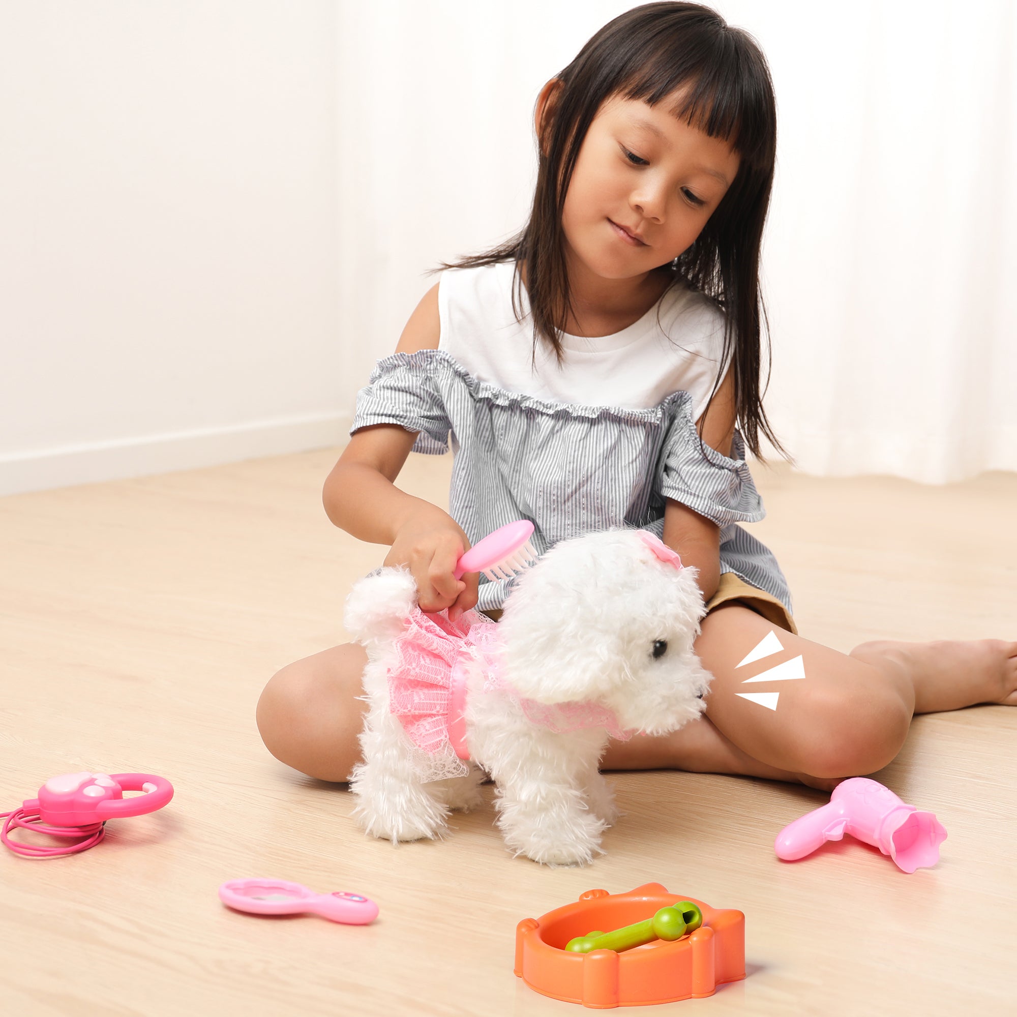 A young girl brushing a white walking puppy toy wearing a pink dress. The puppy is surrounded by grooming accessories, including a hairdryer, brush, and feeding bowl, creating a playful and nurturing scene.