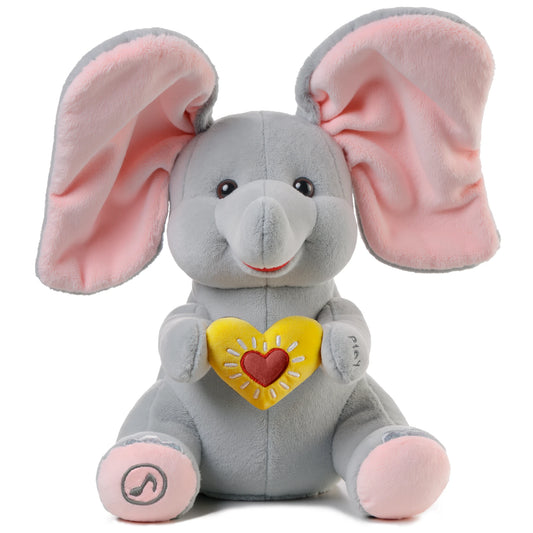 Animated Flappy the Elephant plush toy with large pink ears, holding a yellow heart with a red center. The toy features embroidered 'play' text on one hand and a music note symbol on one foot, indicating interactive singing and ear-flapping functions. Designed as a soft, huggable gift for babies and toddlers.