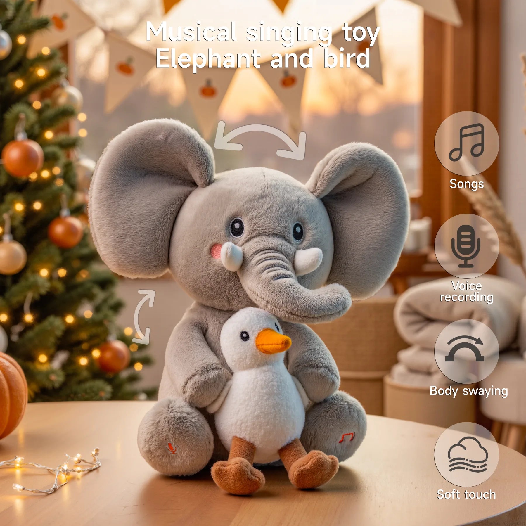 Interactive elephant and bird plush toy sitting on a table in a cozy Christmas setting, with icons showing features like songs, voice recording, body swaying, and soft touch.
